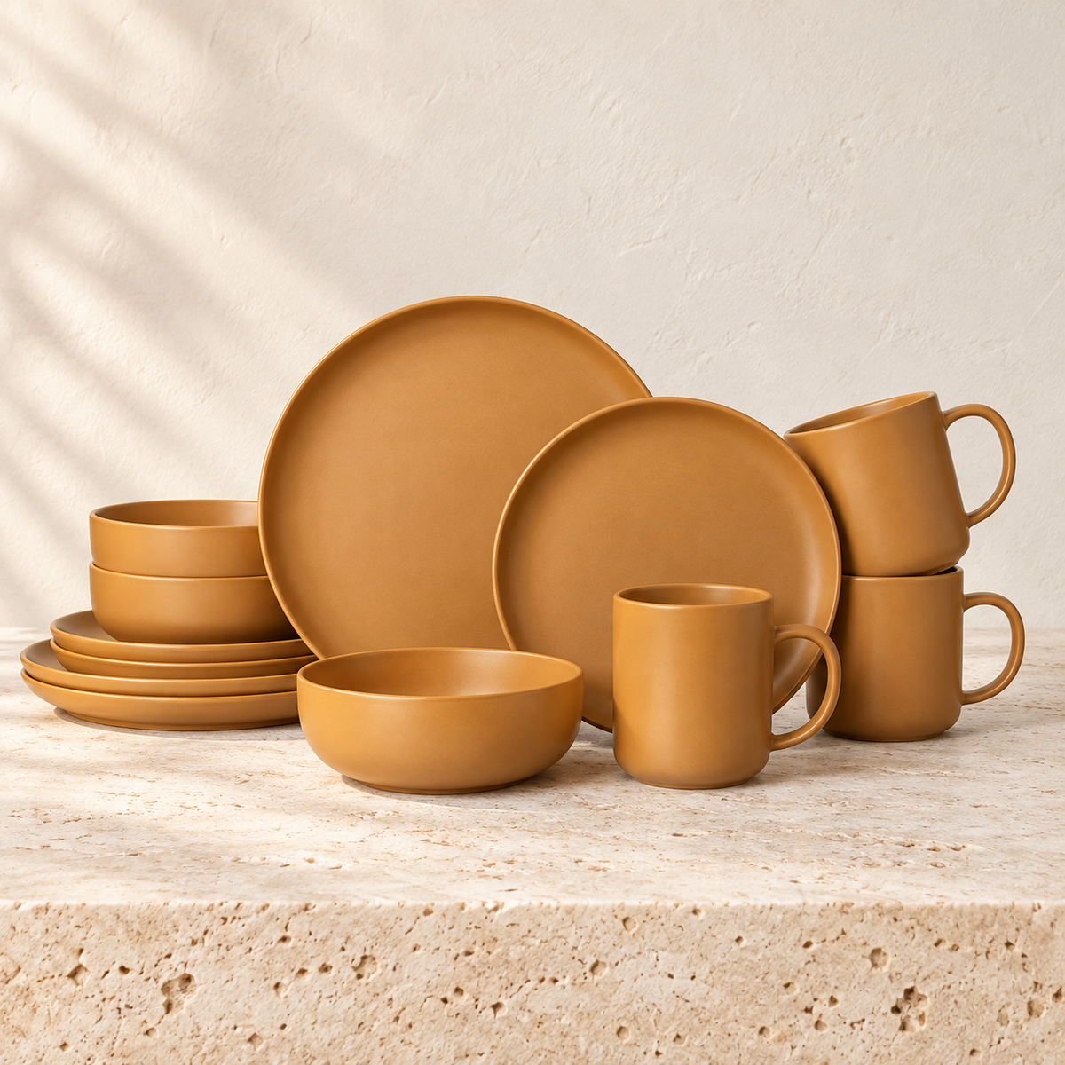 Ochre matte orange stoneware plates, bowls and mugs arranged on a pale stone surface