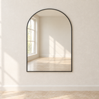 Arc black metal-frame arched wall mirror reflecting a sunlit room