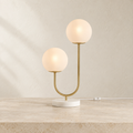 Orbe double-globe lamp lit on a pale surface, with brass-tone stem and white base