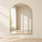 Arc gold-tone arched wall mirror mounted on a pale wall