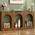 Warm wood arched console table styled with baskets, decorative vases, books, flowers, and brass candleholders against a green wall.