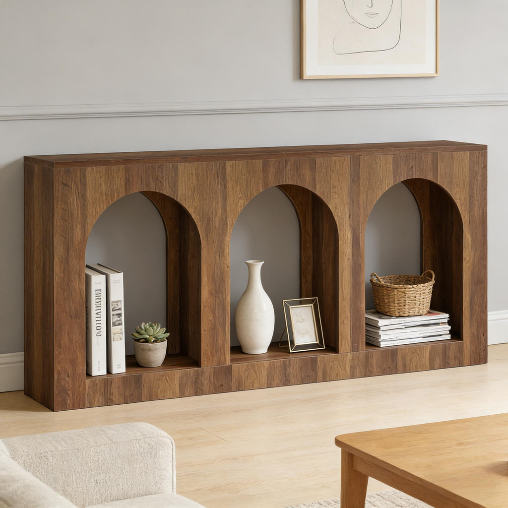 Warm wood arched console table styled with books, a plant, vase, picture frame, basket, and magazines in a minimalist living room.