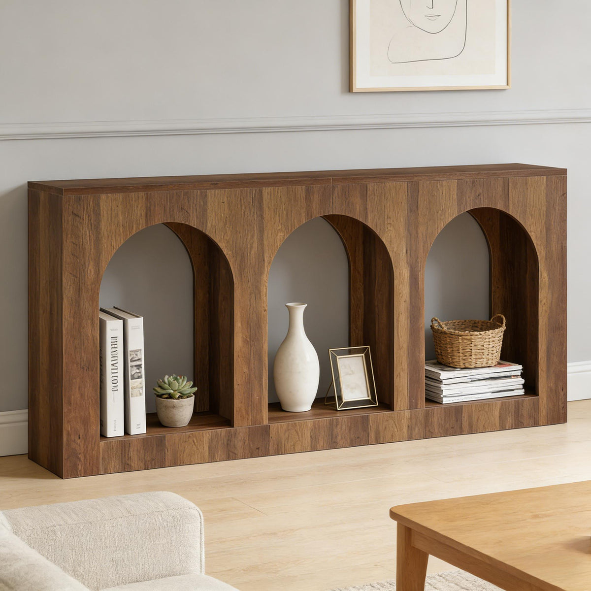 Warm wood arched console table styled with books, a plant, vase, picture frame, basket, and magazines in a minimalist living room.