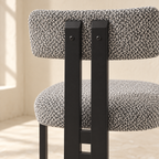 Nola dining chair rear supports in black metal beneath a curved upholstered back