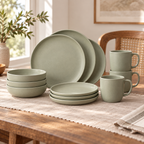 Sage green stoneware plates, bowls and mugs arranged on a dining table