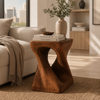 The Sculpt wood accent table styled with books and a ceramic vase beside a neutral living-room sofa.